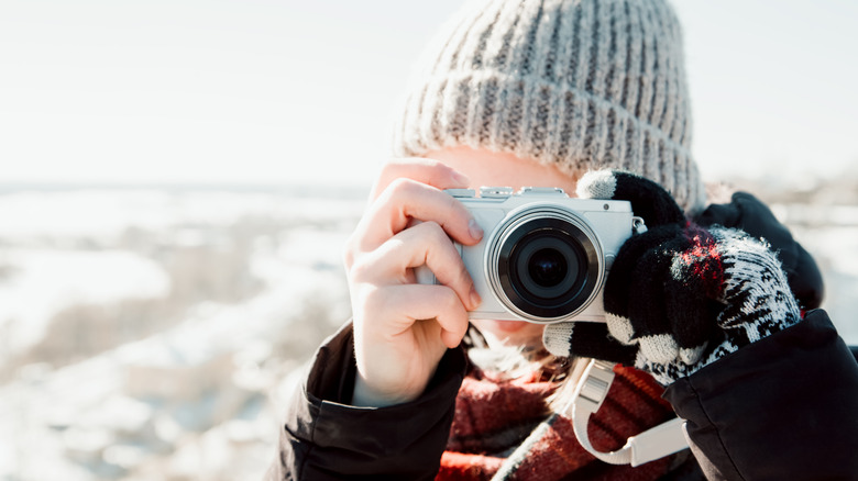 A person using a small silver point-and-shoot digital camera at a sunny beach.