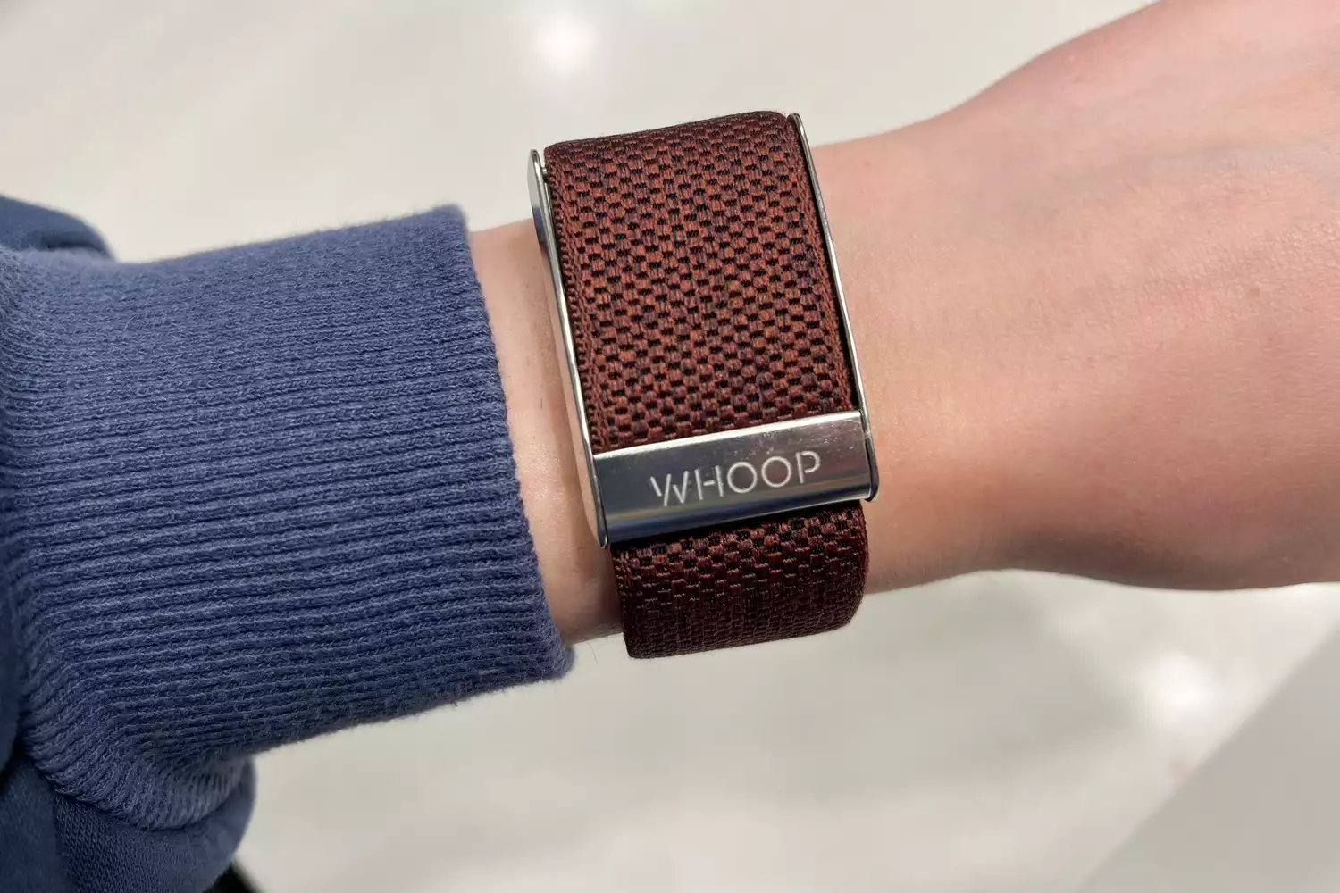 Close-up of a person's wrist wearing a Whoop tracker with a brown woven strap.