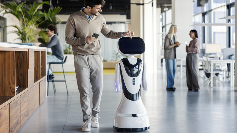A sleek white service robot interacting with a person in a high-tech office environment.