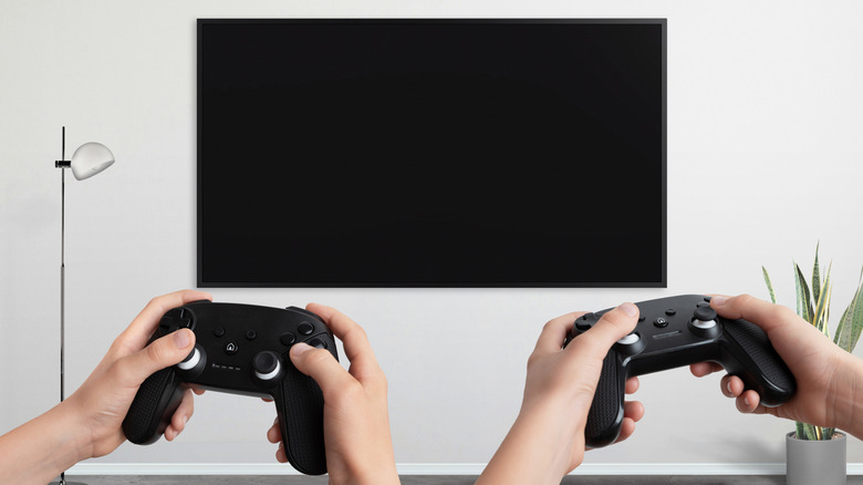 Two players holding game controllers while looking at a large screen TV.