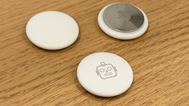 Three circular white Apple AirTags resting on a dark wooden surface.