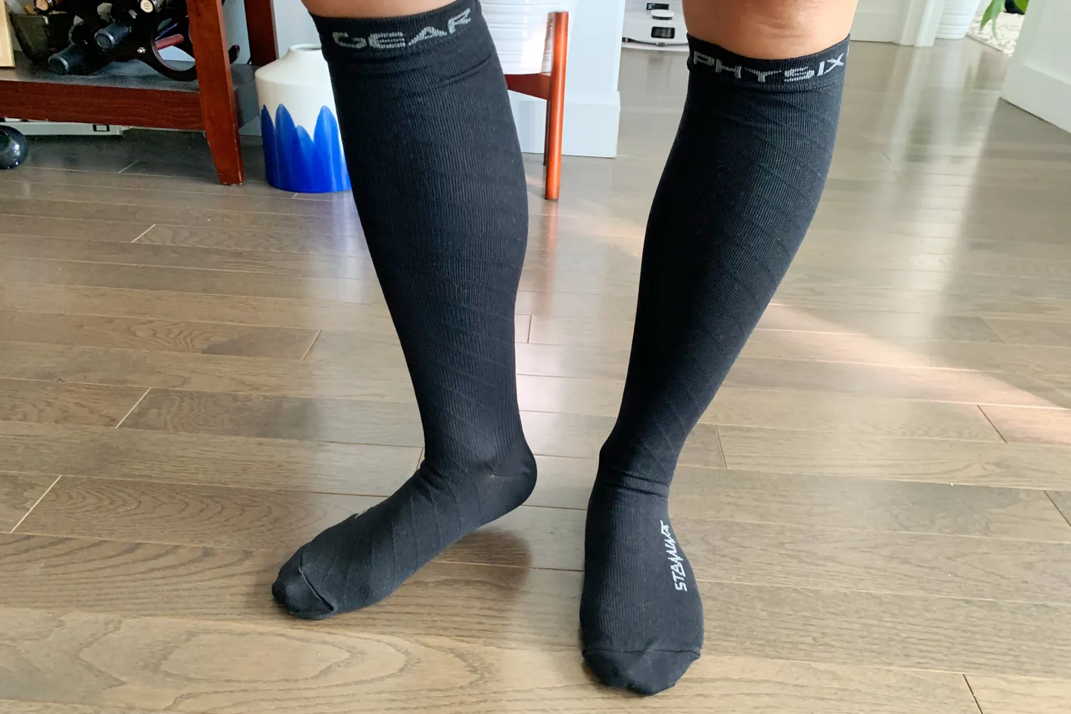 A person standing on a hardwood floor wearing black Physix Gear Sport compression socks.
