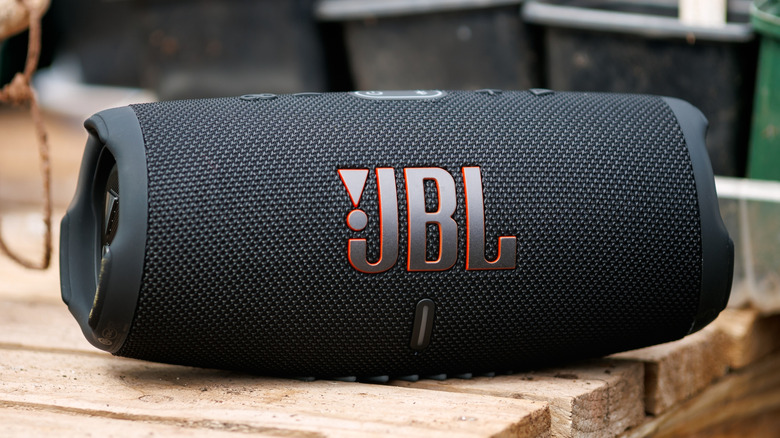 A JBL portable Bluetooth speaker placed on a wooden table in an outdoor setting.