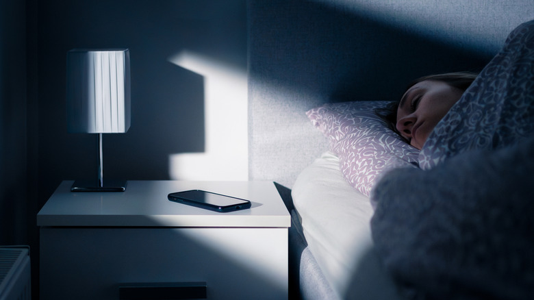 Woman sleeping in bed with a smartphone placed on the nightstand next to her head.