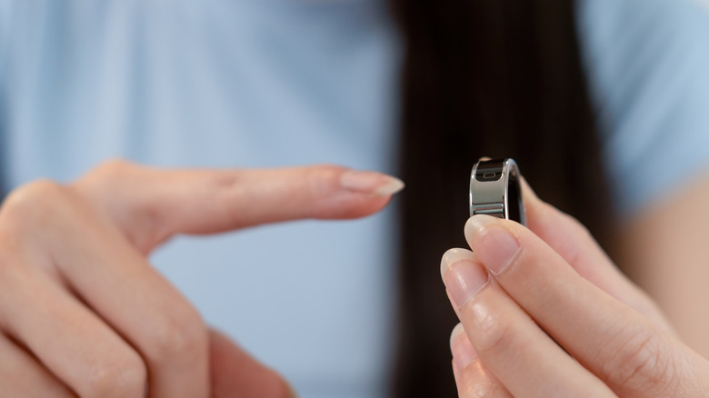 A woman holding a smart ring and examining her finger for the correct fit.