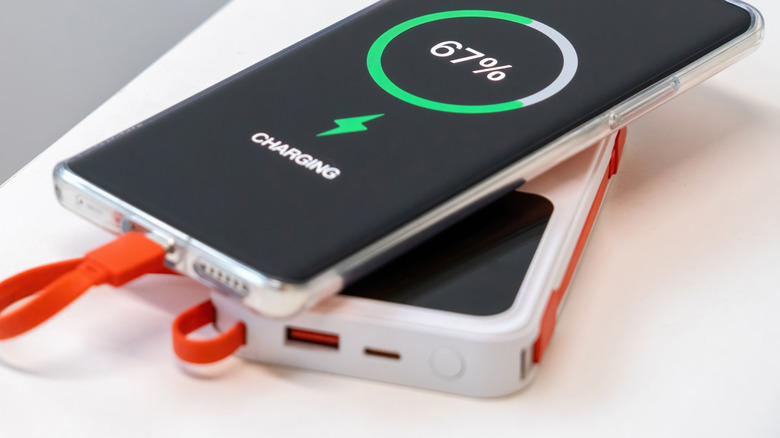 A smartphone being charged by a portable power bank on a flat surface.