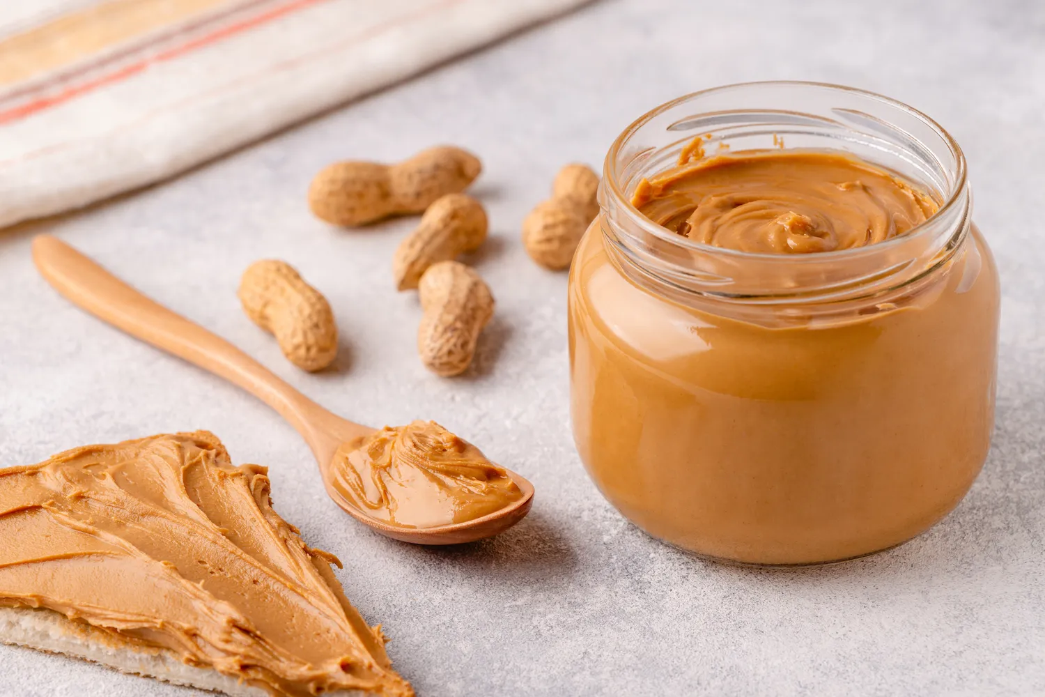 Creamy peanut butter being scooped from a jar with a wooden spoon.