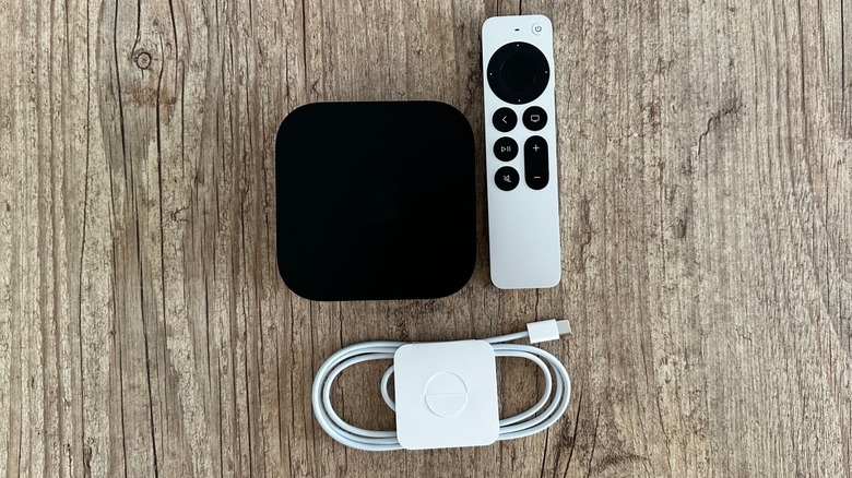 Top-down view of the Apple TV 4K console, the Siri Remote, and a USB-C charging cable on a flat surface.