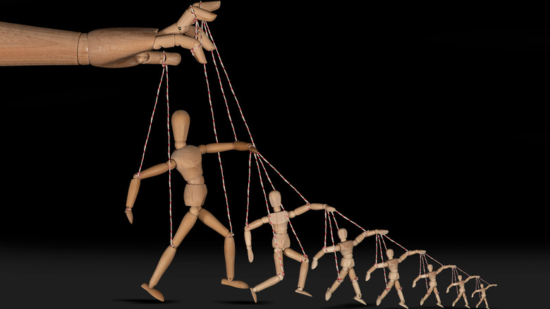 A row of wooden puppet dolls connected by strings, symbolizing manipulation.