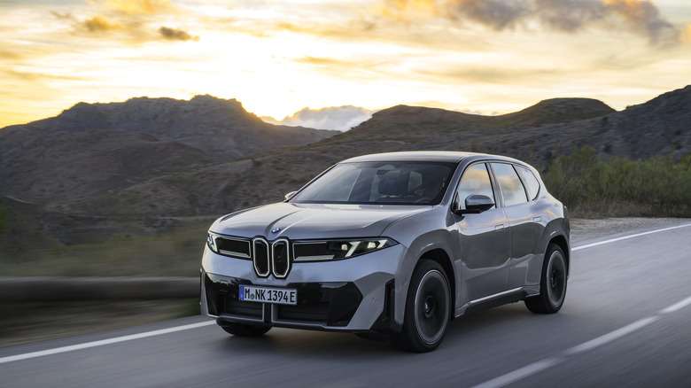 Front left view of a grey BMW iX3 driving on a mountain highway.