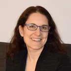 A professional woman in a black blazer and glasses representing a health expert or nutritionist.