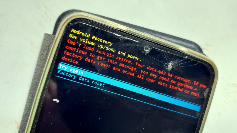 A cracked smartphone screen displaying the Android system recovery menu with factory reset options.