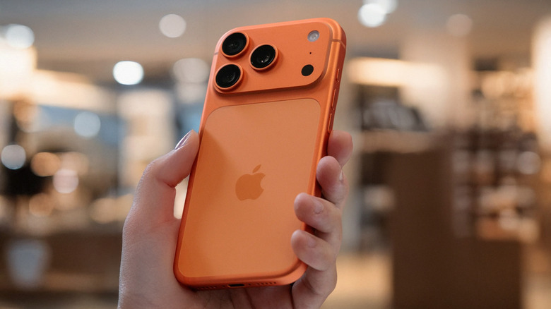 A person holding an orange iPhone 17 Pro Max at an angle to show the lens depth.